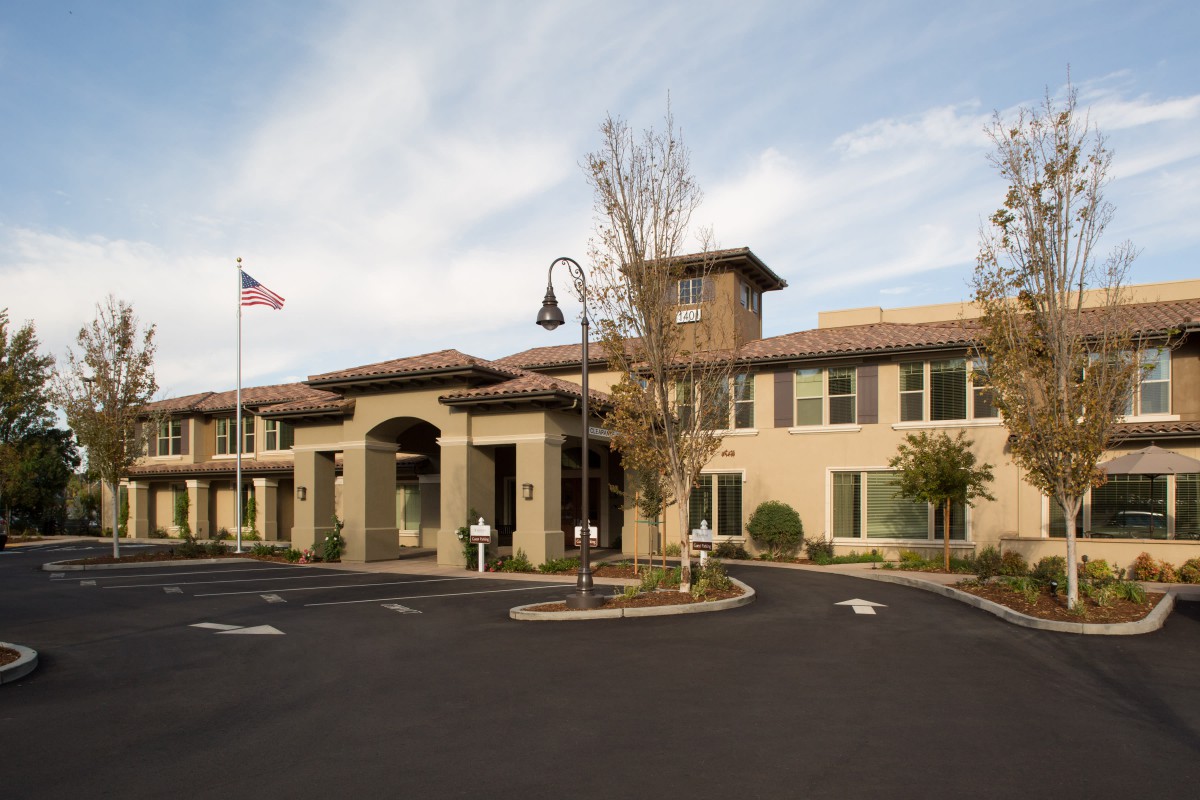 A modern building with a prominent entrance, surrounded by a parking lot and landscaped trees.
