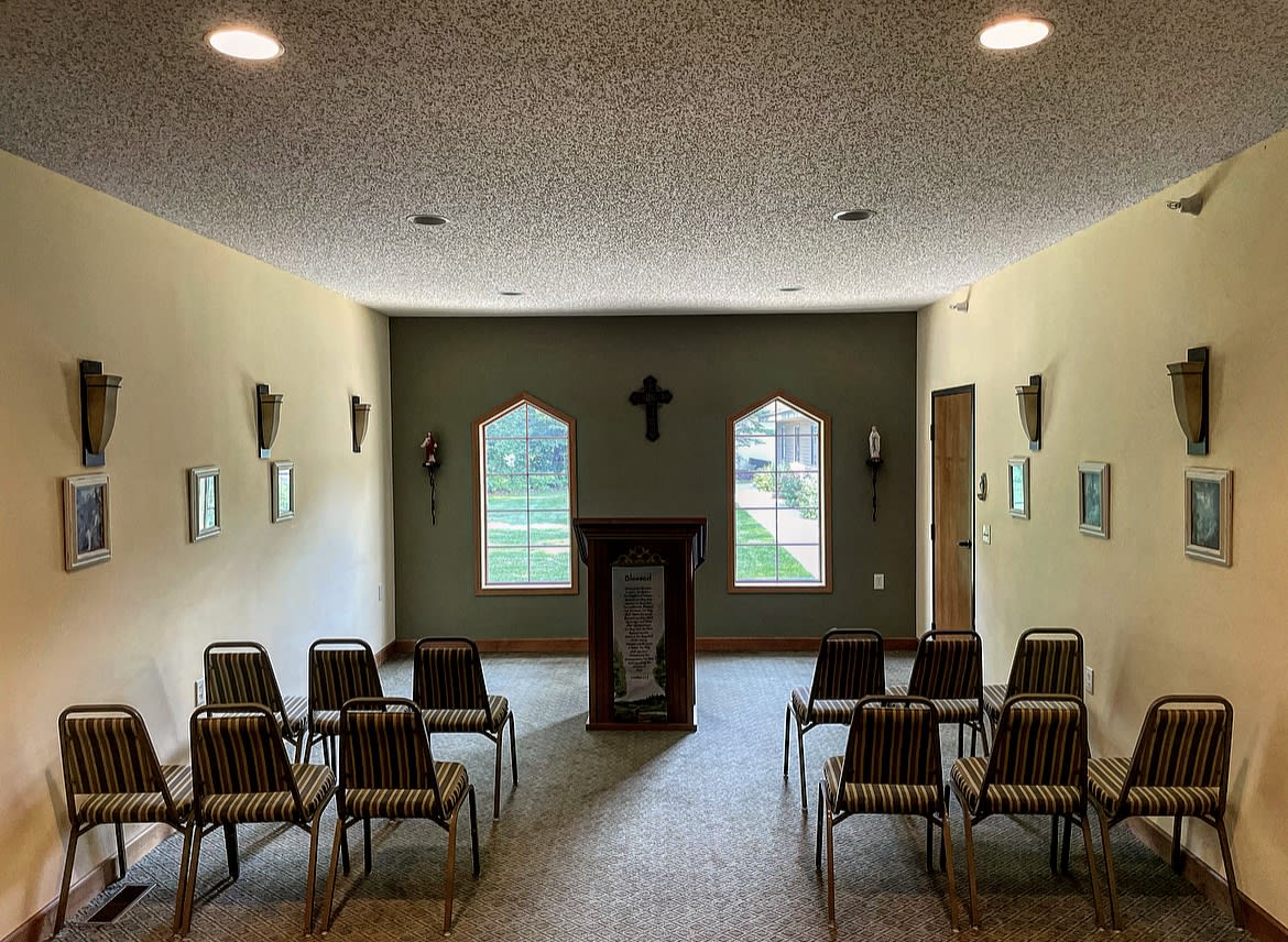 A small chapel with chairs arranged in rows facing an altar and cross under two windows.