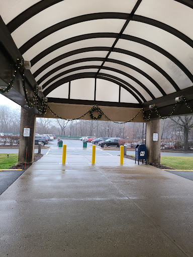 A covered entrance leading to a parking area, featuring yellow barriers and a view of the surrounding trees under overcast skies.