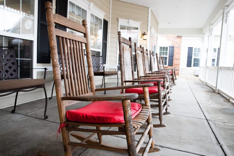 A row of wooden rocking chairs with red cushions on a porch.