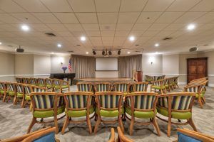 An empty conference room with rows of chairs facing a stage and projector screen.