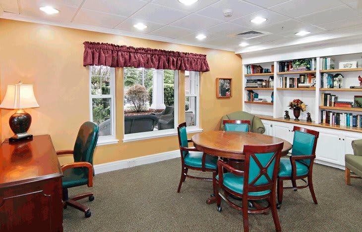A cozy meeting room with a round table, chairs, and a bookshelf by the window.