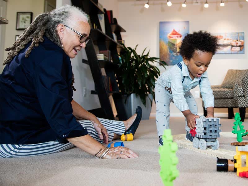 A grandparent and child enjoy playing with toys on the floor indoors.