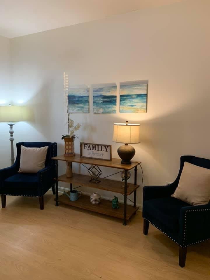 A cozy living room setup with two chairs, a small table adorned with lamps and decorations, and artwork on the wall.