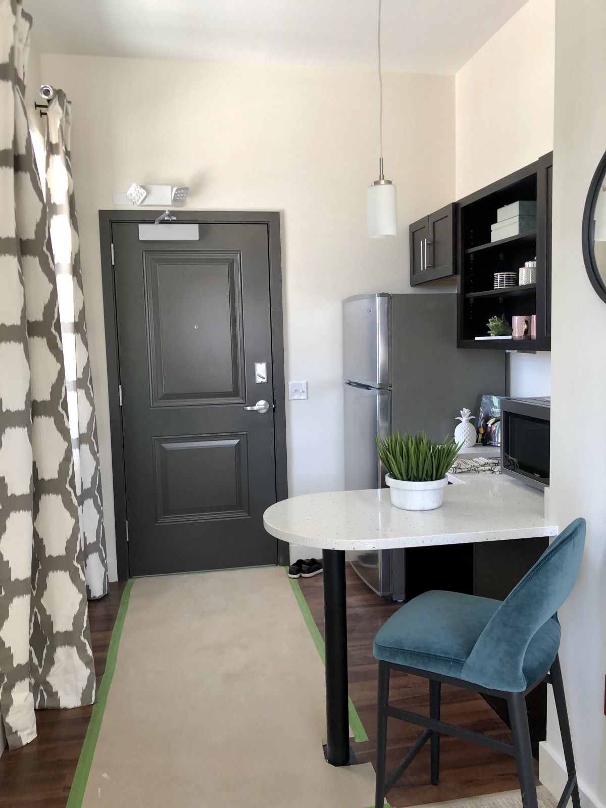 A modern kitchen area in an apartment featuring a refrigerator, bar stool, and decorative items.