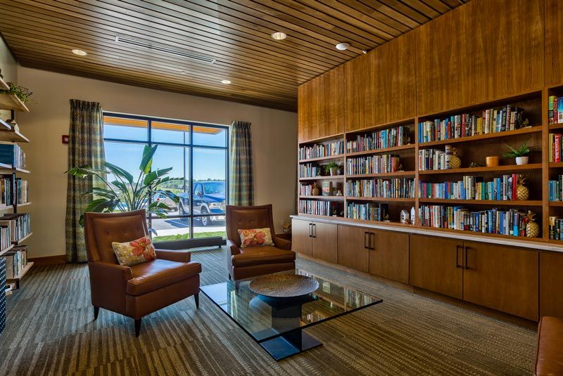 A cozy library with wooden bookshelves and armchairs overlooking a coastal view through a large window.