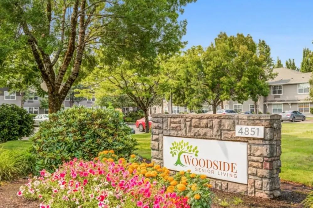 A beautifully landscaped entrance to the Woodside apartment complex, featuring colorful flowers and lush trees.