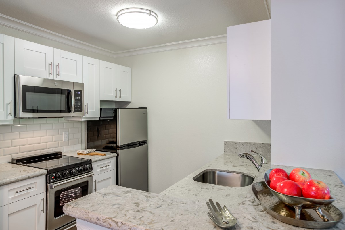 A modern kitchen featuring stainless steel appliances, white cabinets, and a compact layout.