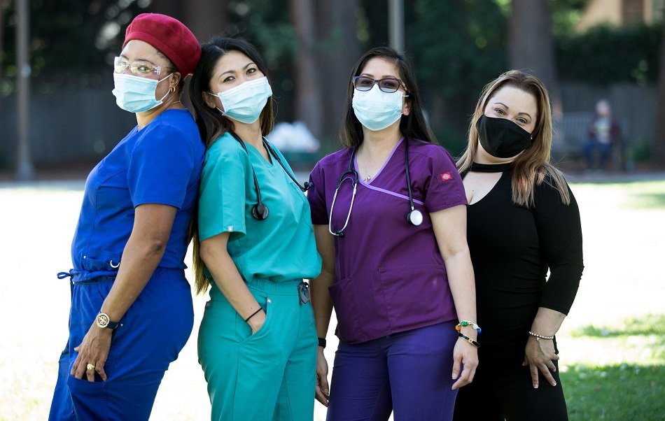 A group of healthcare professionals in scrubs and masks posing outdoors.