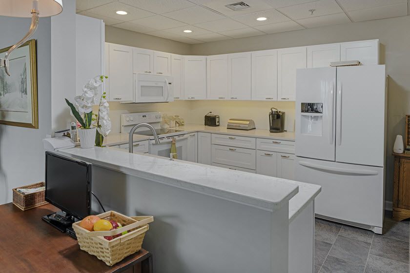 A modern kitchen with white cabinets and a clean countertop, featuring appliances and a fruit basket.