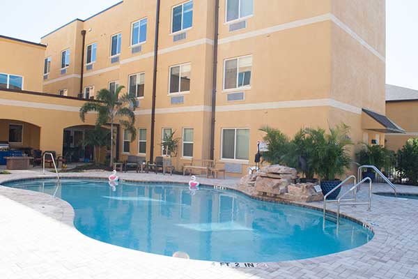 An outdoor swimming pool area with surrounding hotel building and palm trees.