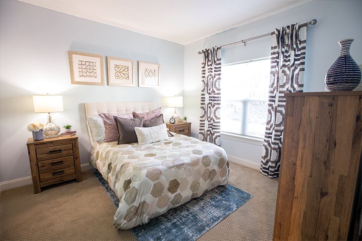A cozy and well-decorated bedroom with a bed, wooden nightstands, patterned curtains, and framed artwork on the wall.
