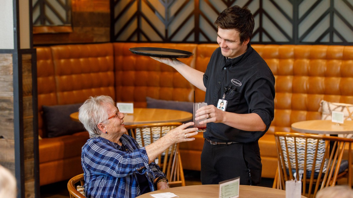 A server handing a drink to a customer at a restaurant.