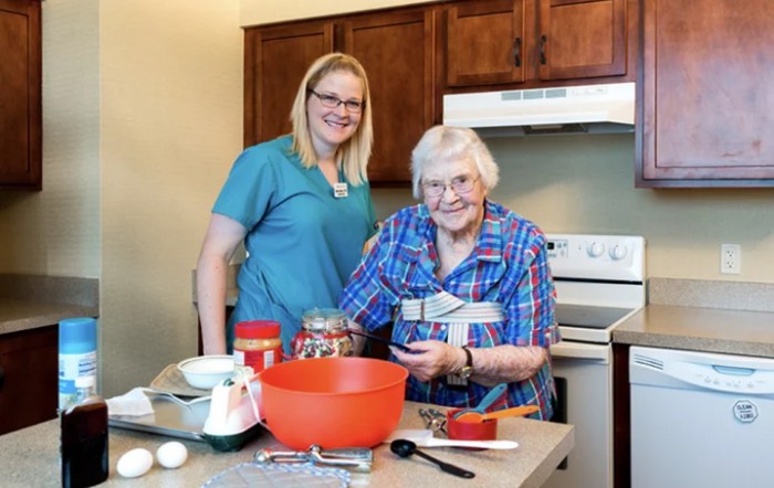 Two women smiling while preparing food in a kitchen.