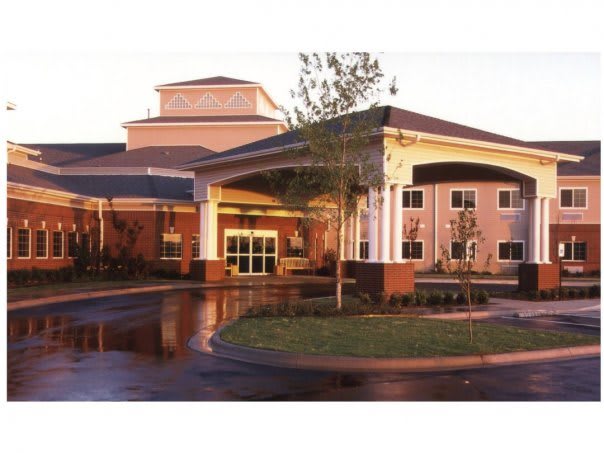 A modern building with a covered entrance and columns, surrounded by trees in the evening light.
