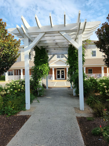 A beautiful entrance framed by a white pergola, leading to a charming house surrounded by lush greenery.