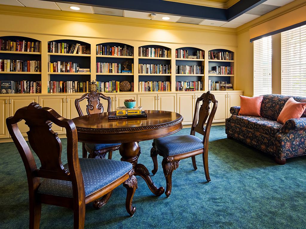 A cozy library room with bookshelves, a round table, chairs, and a sofa.