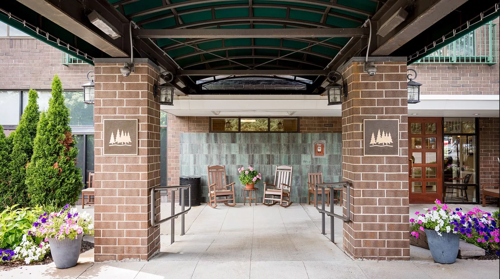 The entrance features a brick walkway with a canopy, flanked by rocking chairs and plants.