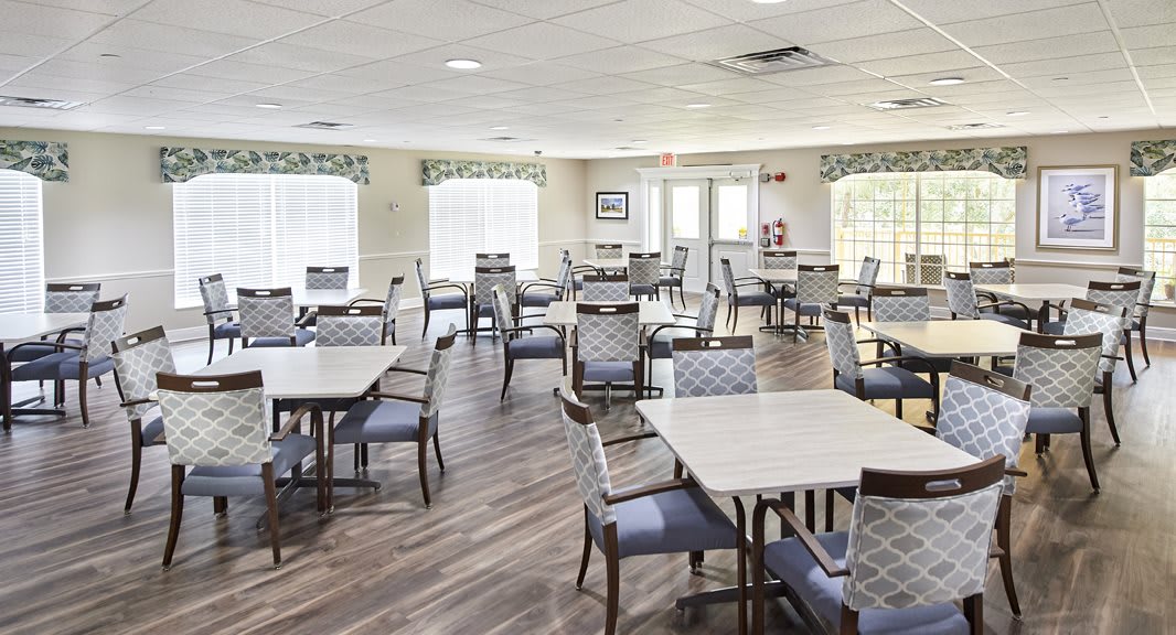 A bright and spacious dining area with multiple tables and chairs arranged on a wooden floor.