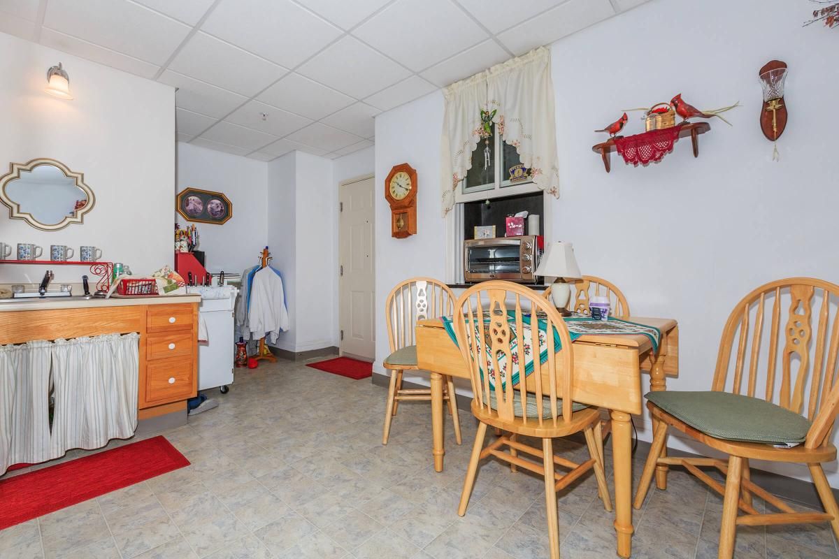 A cozy kitchen dining area with a wooden table, chairs, shelves, and decorative elements.
