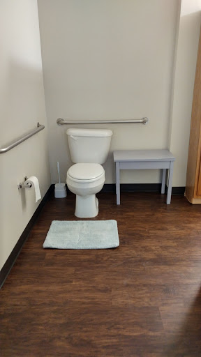 A clean and accessible bathroom setup featuring a toilet, grab bars, and a floor mat.