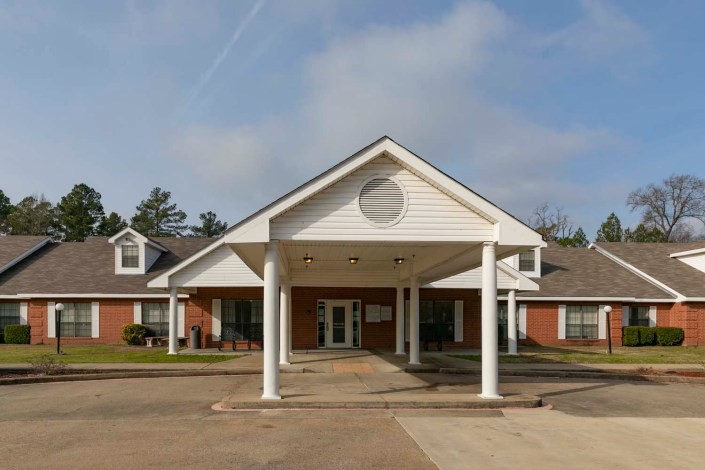 A building entrance with prominent columns and a peaked roof under a cloudy sky.