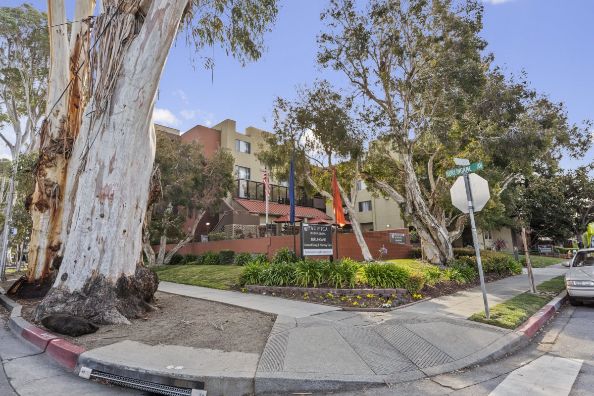 A residential building surrounded by trees at a street corner with a stop sign and sidewalk.