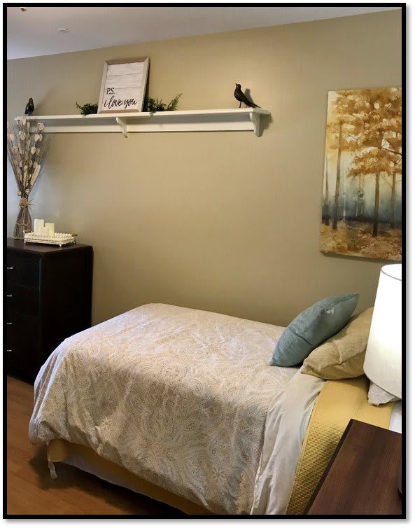 A cozy bedroom with a single bed, a shelf displaying decor, and a painting on the wall.