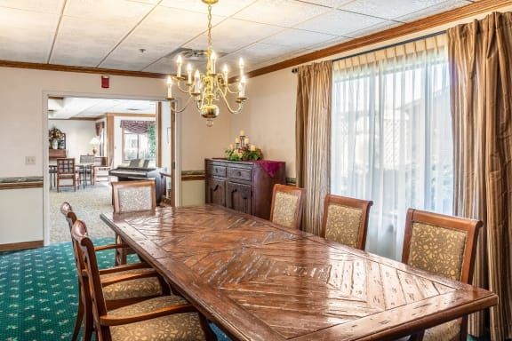 A well-lit dining room with a large wooden table, surrounded by chairs and a chandelier overhead.
