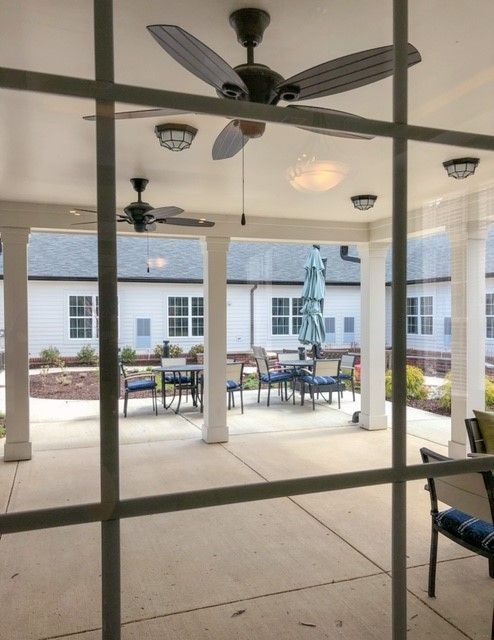 A cozy patio area with outdoor seating, ceiling fans, and protective columns under a covered roof.