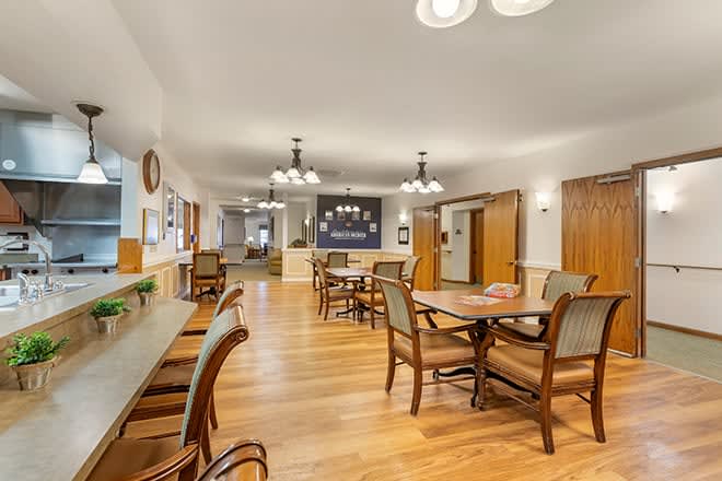 A spacious dining area with wooden floors and various tables and chairs arranged neatly under elegant lighting fixtures.