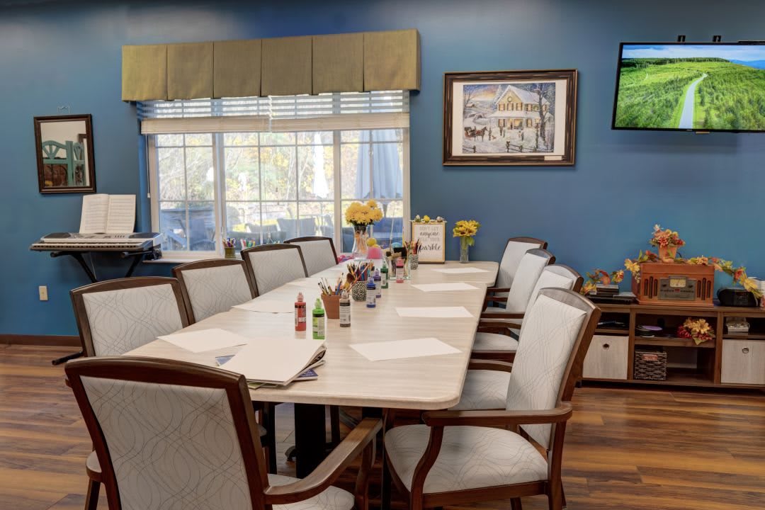 A conference room with a long meeting table, surrounded by chairs, notepads, and bottles of hot sauce on the table. The room has blue walls, large windows with blinds, and a decorative painting on the wall.