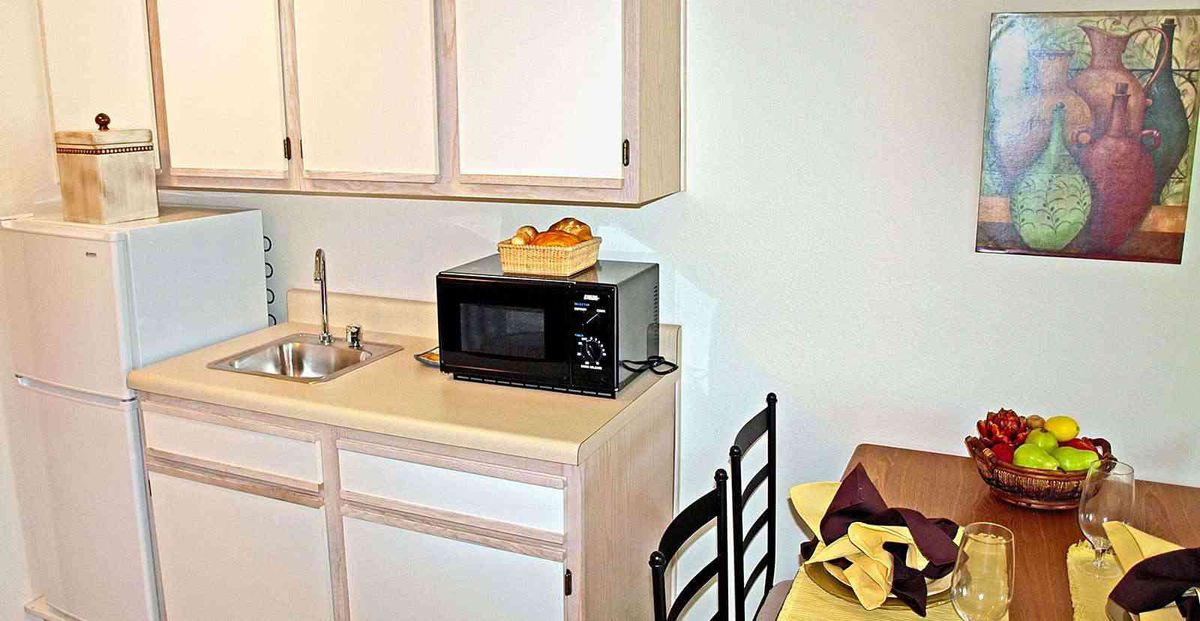 A small kitchen area featuring a microwave on the countertop, surrounded by cabinets and a dining table with chairs.