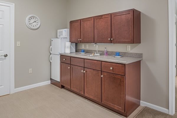 A small kitchenette with wooden cabinets, a refrigerator, microwave, and sink.