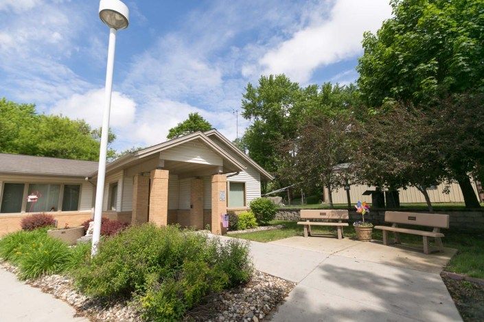 A suburban house with well-maintained landscaping, featuring a bench and a driveway under a partly cloudy sky.