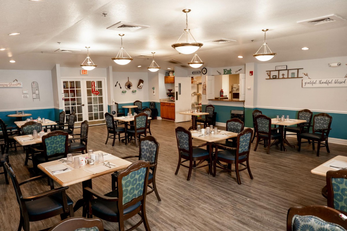 A spacious and elegantly decorated dining room with multiple tables and chairs, featuring soft lighting and wooden flooring.