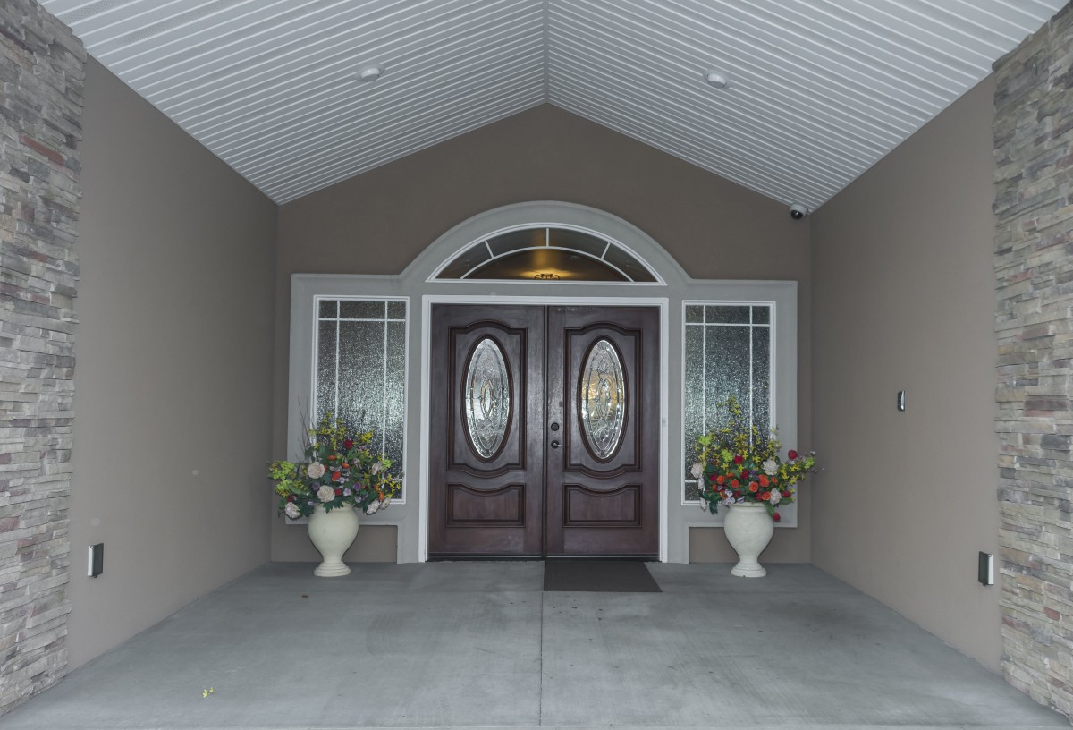 An elegant entrance with double wooden doors and potted plants on either side.