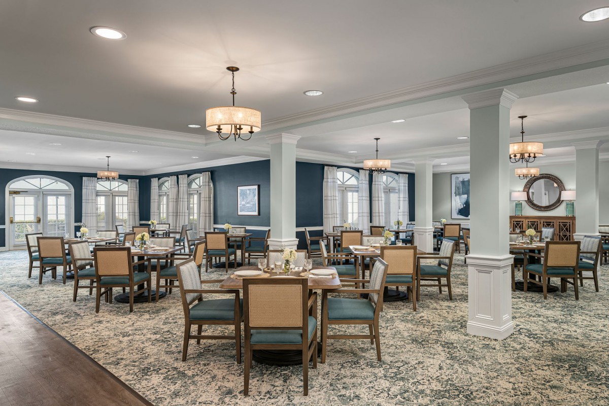 A spacious and elegant dining room with multiple tables and chairs, featuring chandeliers and large windows.