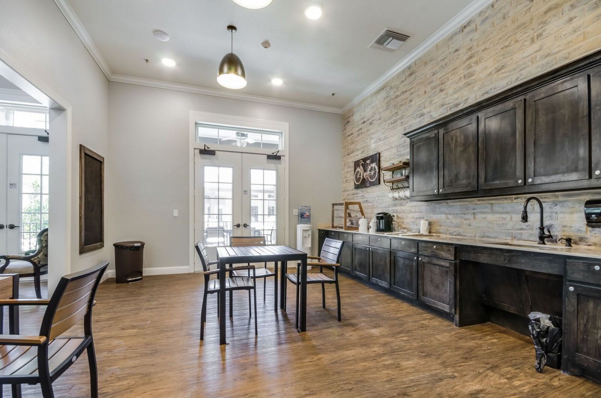 A modern kitchen and dining area featuring a wooden table, chairs, and dark cabinets against a brick accent wall.