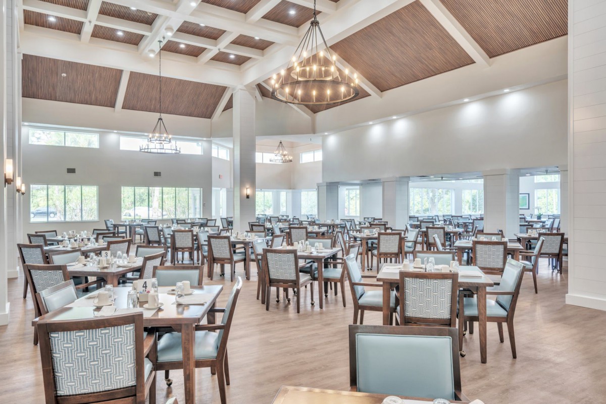 A spacious dining hall with neatly arranged tables and chairs, illuminated by elegant chandeliers.