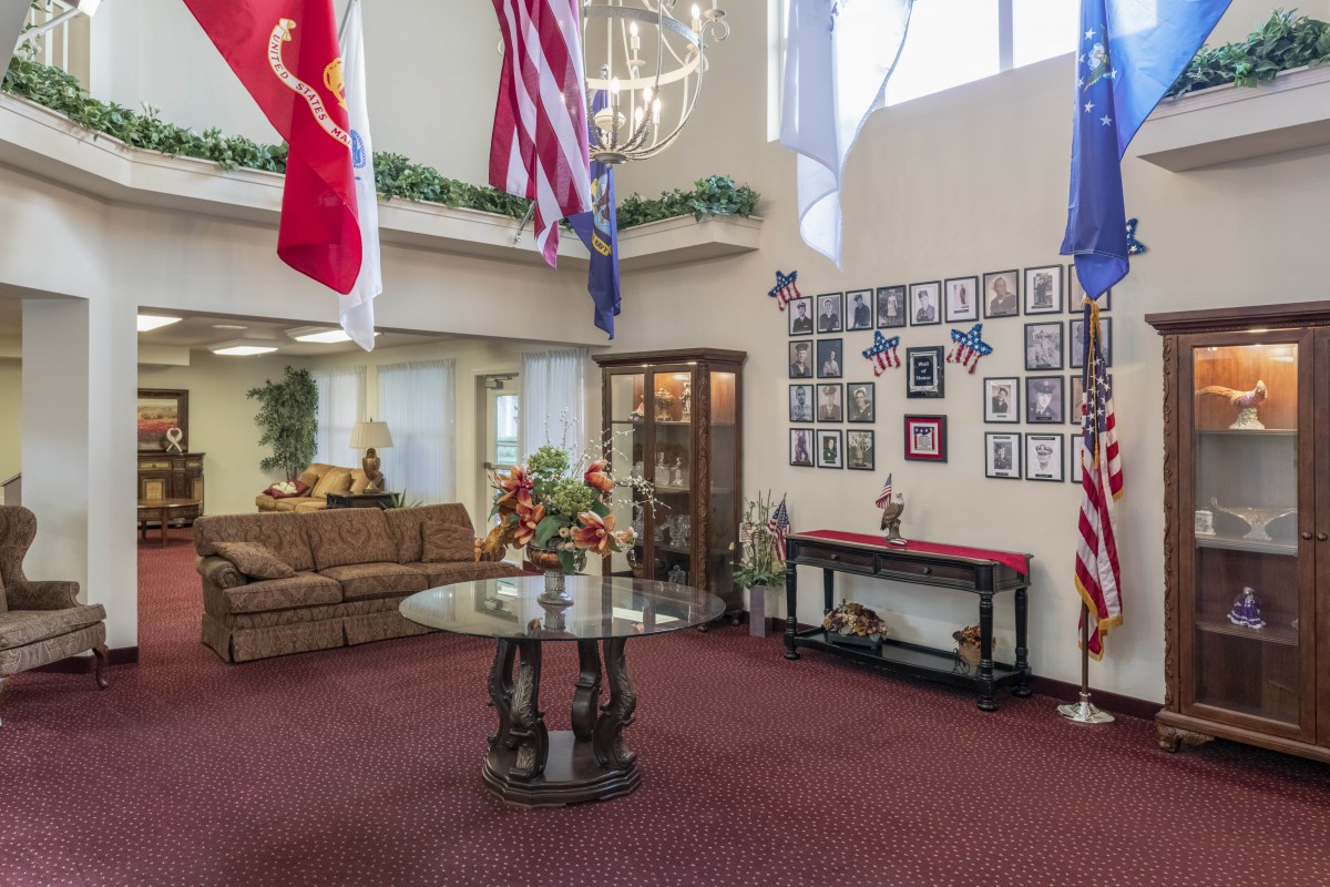 A lobby interior with flags hanging from the ceiling, a sofa, and a table surrounded by pictures on the wall.