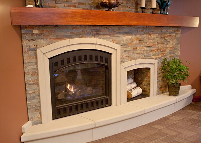 A cozy indoor fireplace with a stone wall, adorned with decor items and neatly stacked logs beside it.