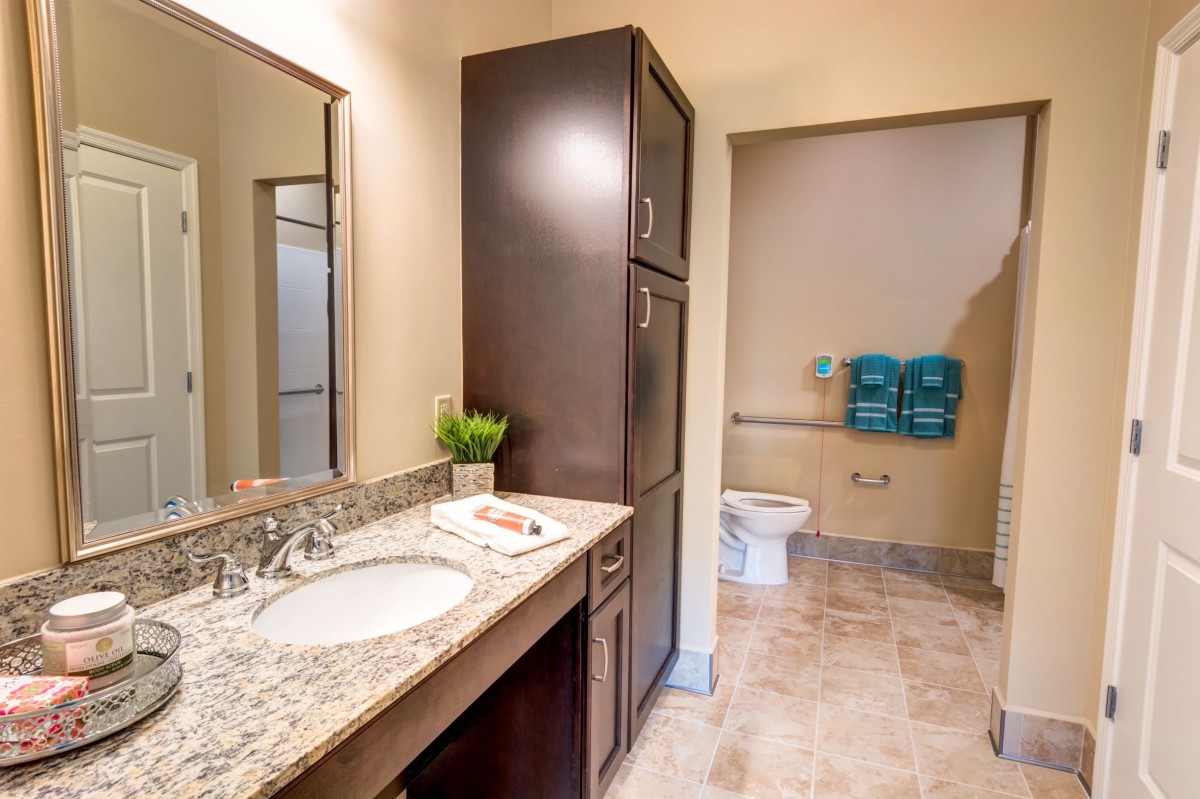 A modern bathroom with a granite countertop, dark cabinetry, and blue towels.