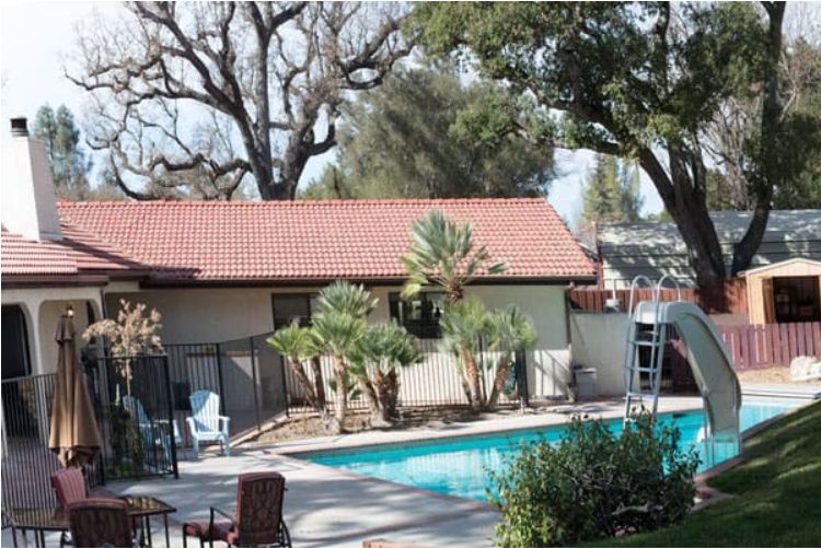 A serene backyard setting with a swimming pool, surrounded by trees and a small house.