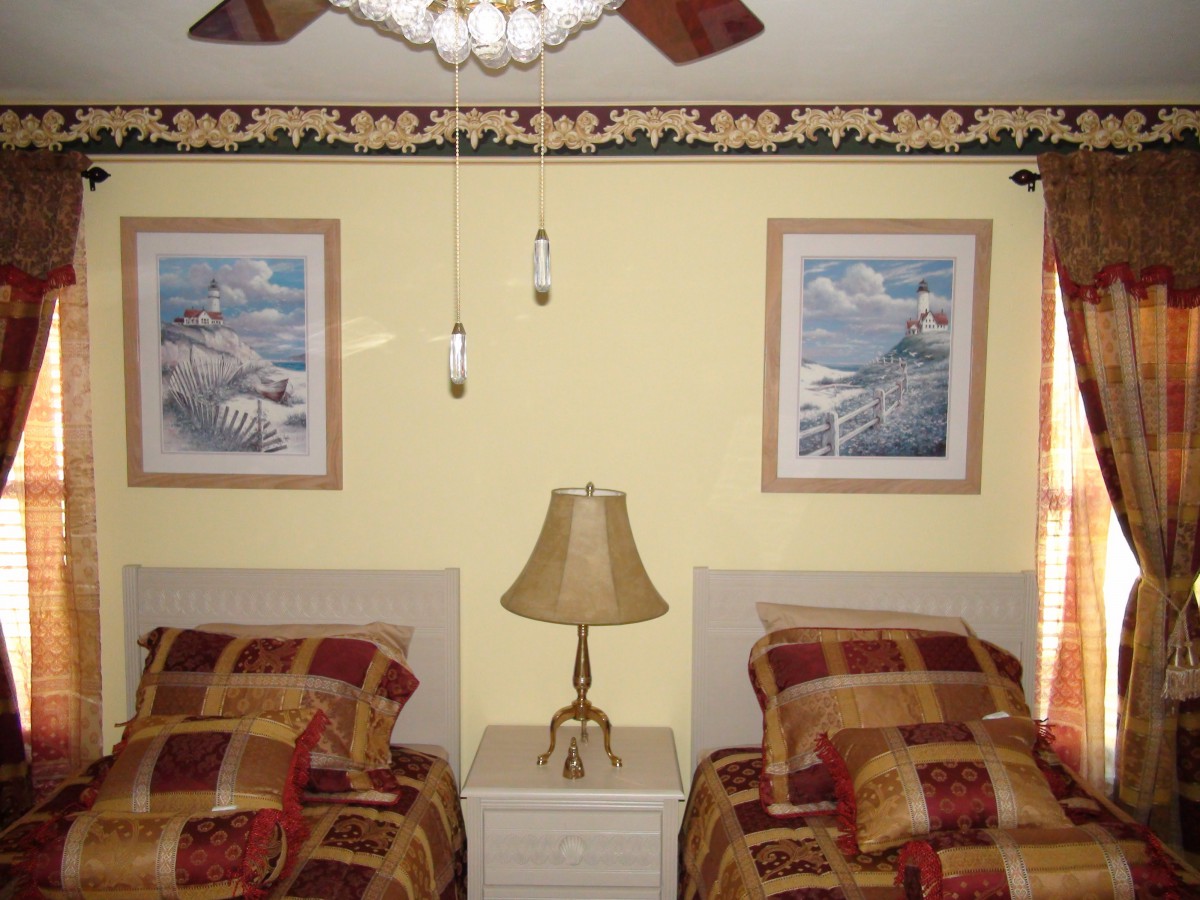 A cozy bedroom featuring twin beds, a lamp on a nightstand, and decorative paintings on the wall.