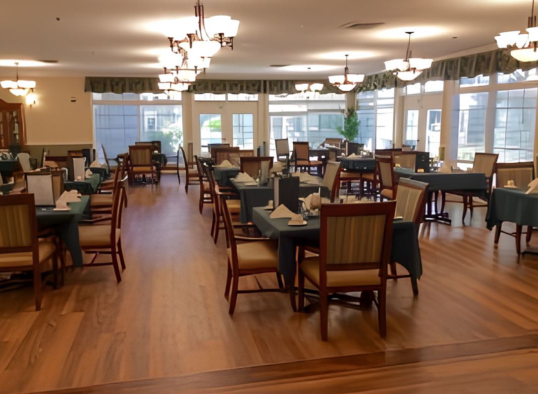 A spacious dining area featuring neatly arranged tables and chairs with elegant chandeliers and ample natural light.