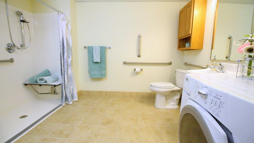 An accessible bathroom with grab bars, a shower, toilet, and a washer.