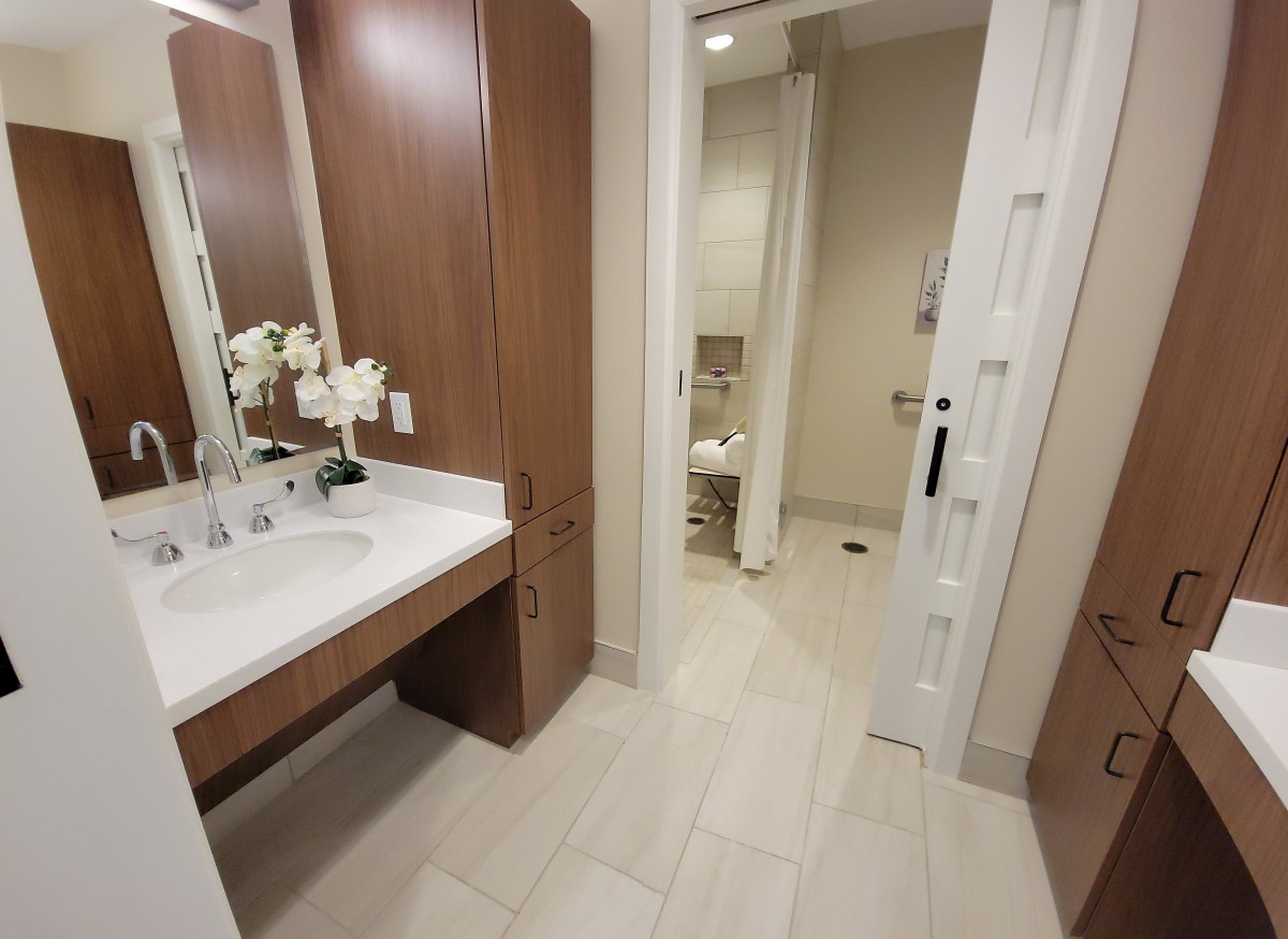 A modern bathroom with a vanity area, featuring wooden cabinets and a tiled floor.