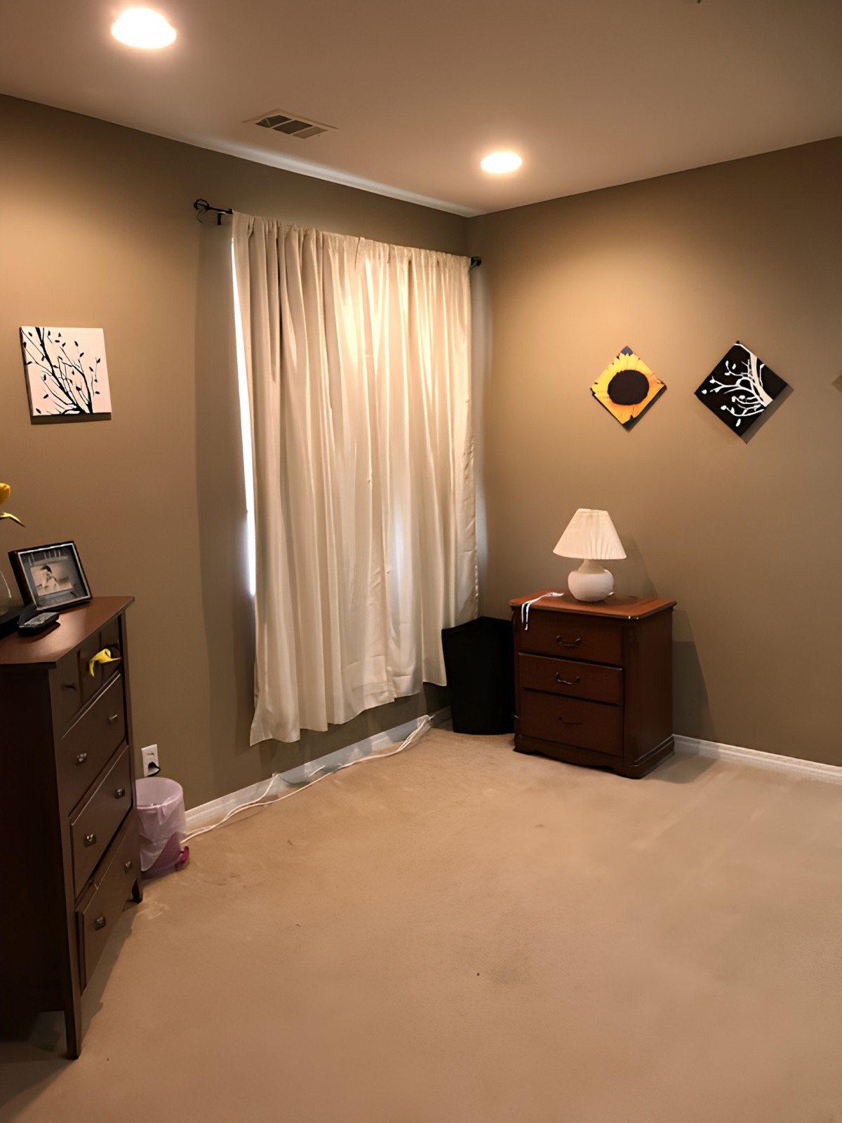 A cozy room with a dresser, lamp, and wall decor.