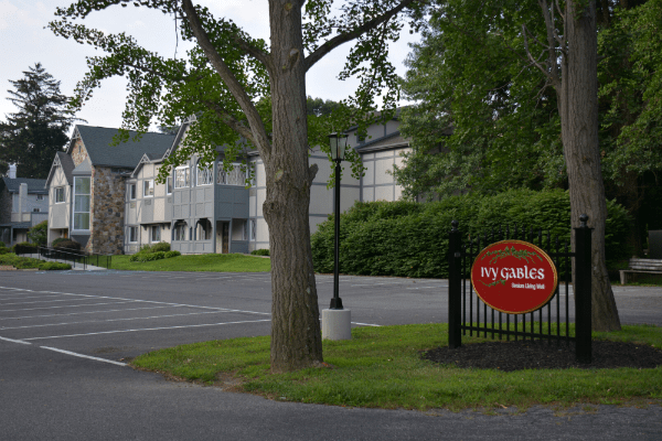 A hotel with a parking lot and sign in a green, outdoor setting.